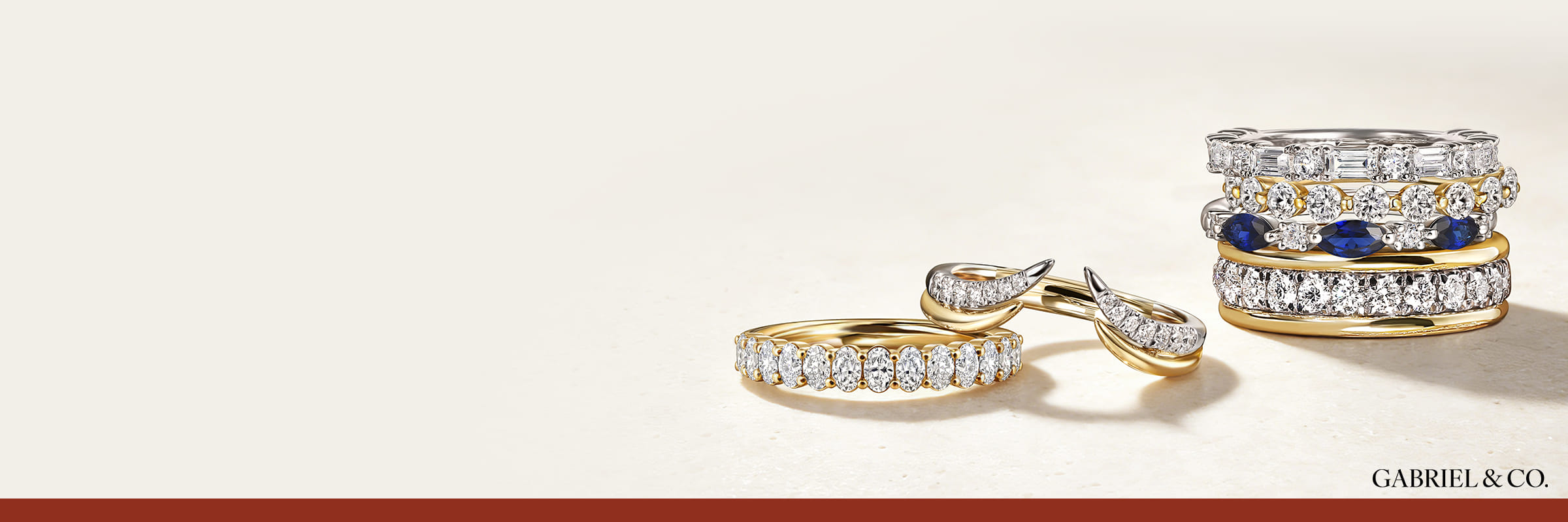 Diamond wedding bands arranged on a cream surface, including an open diamond band, a curved diamond piece, and a stack of bands featuring a sapphire and diamond design.